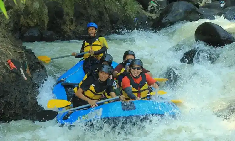 Peserta rafting sedang mengarungi jeram sungai di Bogor menggunakan perahu karet biru dan perlengkapan keamanan lengkap, salah satu paket adventure dari Paintball Bogor.